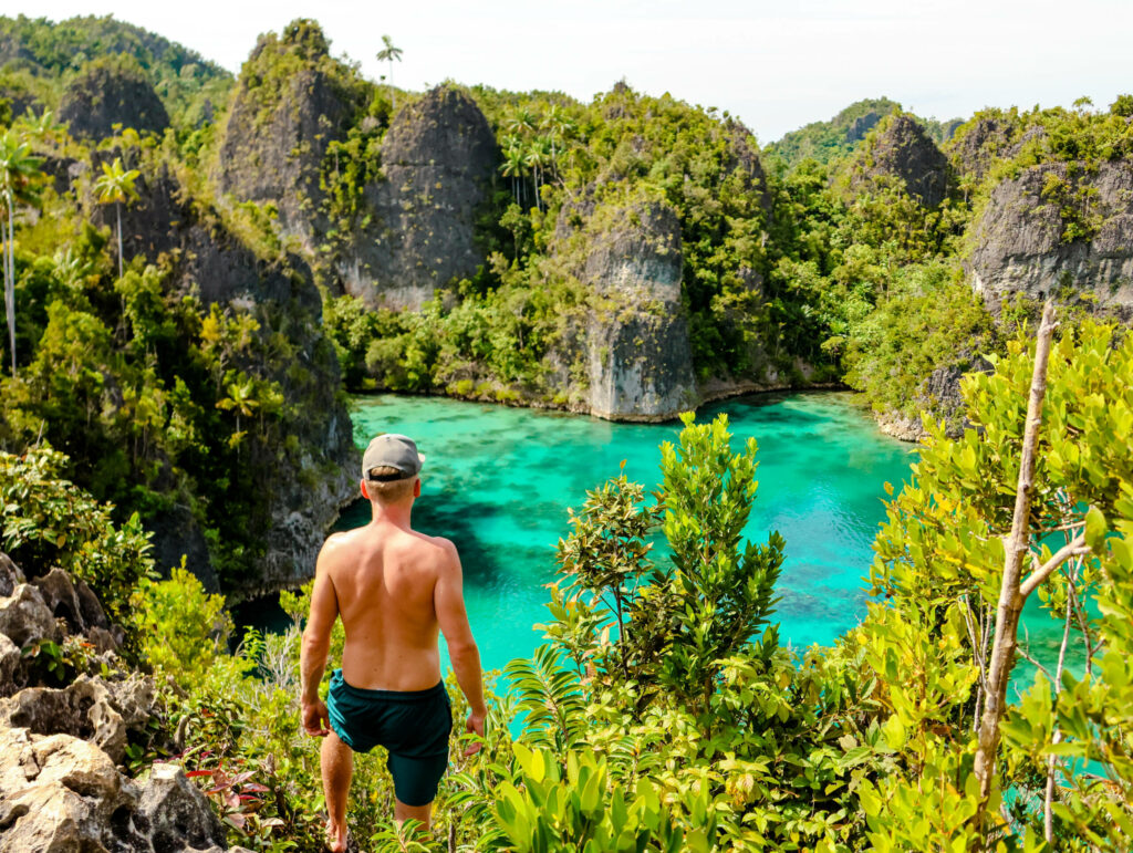 Blogger Tom steht an einer Klippe und blickt über das Meer auf die steinerne Küste der Star Lagoon auf Raja Ampat.