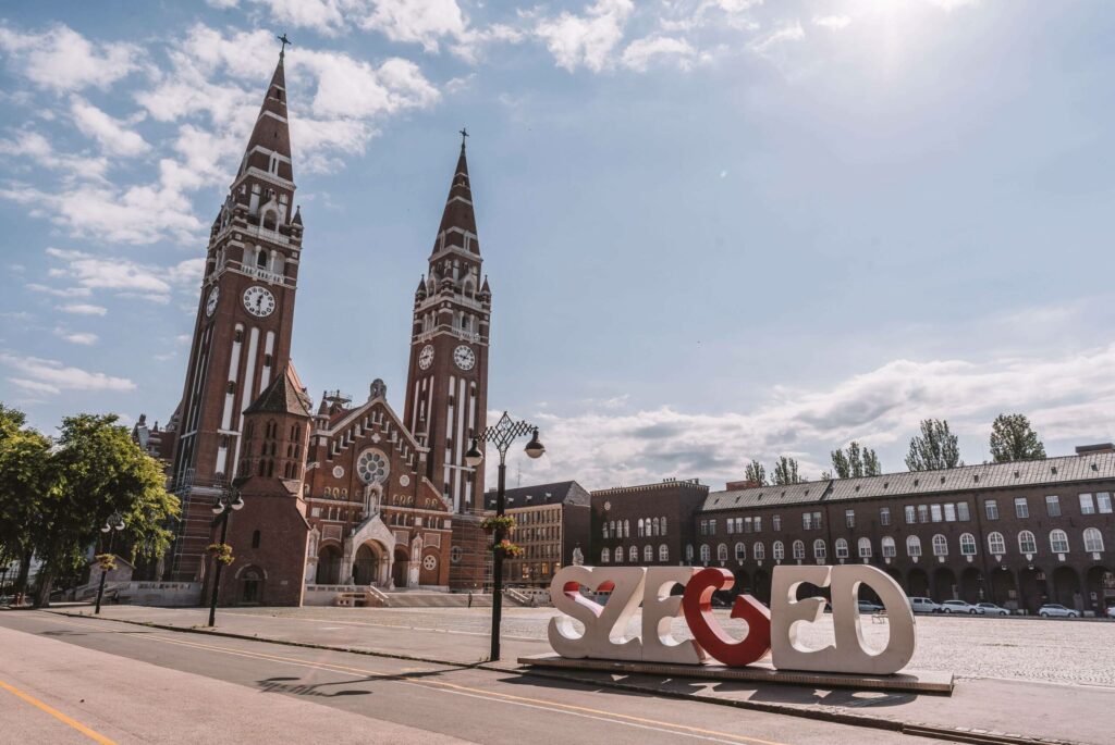 Die braunrote Kathedrale in Szeged mit einem Schriftzug des Stadtnamen in Ungarn.