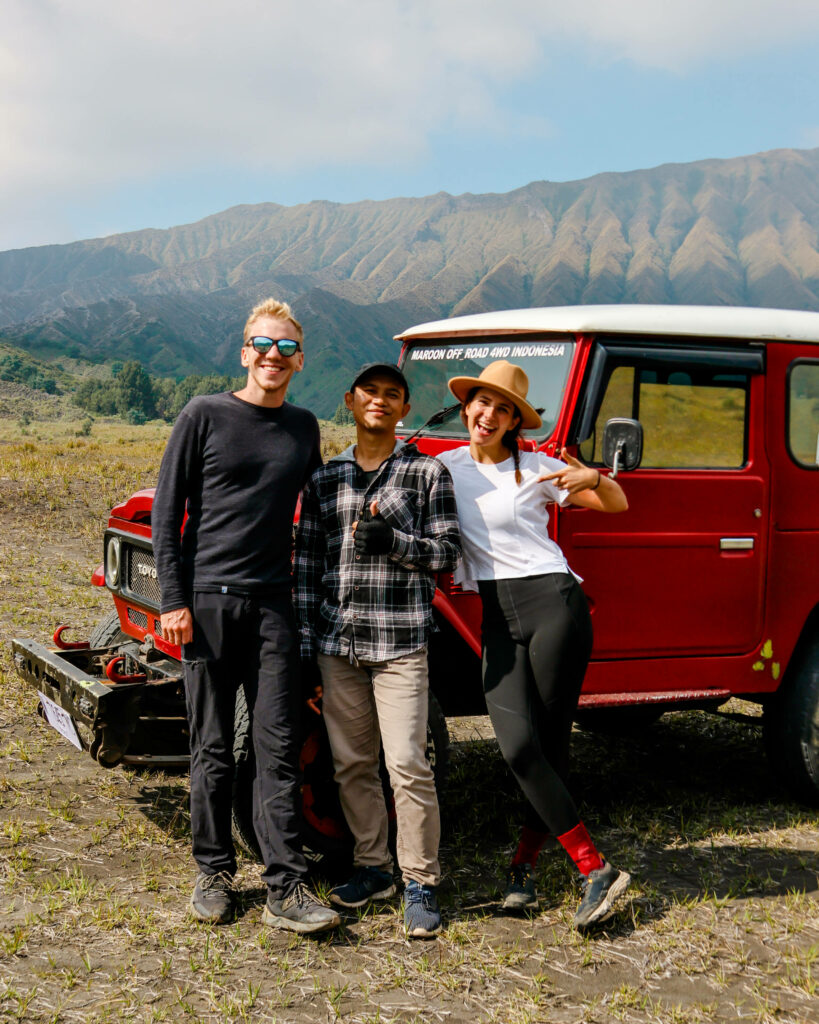 Die Blogger Nina und Tom stehen mit ihrem Tourguide vor einem roten Jeep und posen für ein Foto in Java.