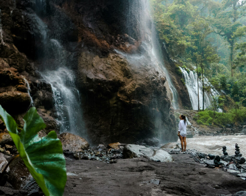 Bloggerin Nina steht am Fuße eines Wasserfalls in Java.