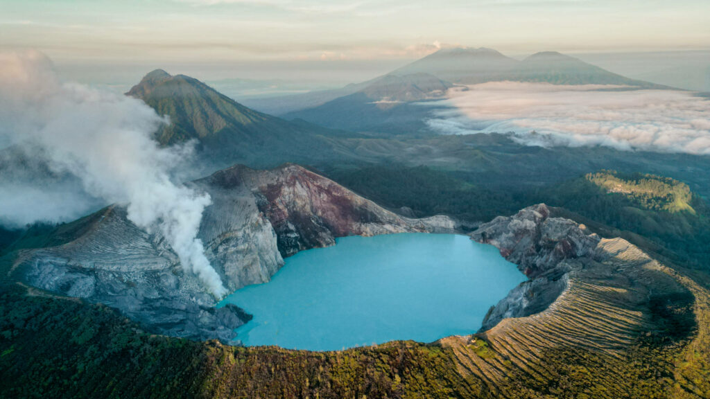 Ein türkisblauer See im Vulkan Ijen in Java, im Hintergrund begrünte Berge.