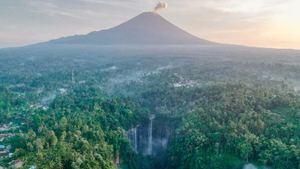Der Tumpak Sewu Wasserfall in Java mit einem Vulkan im Hintergrund.