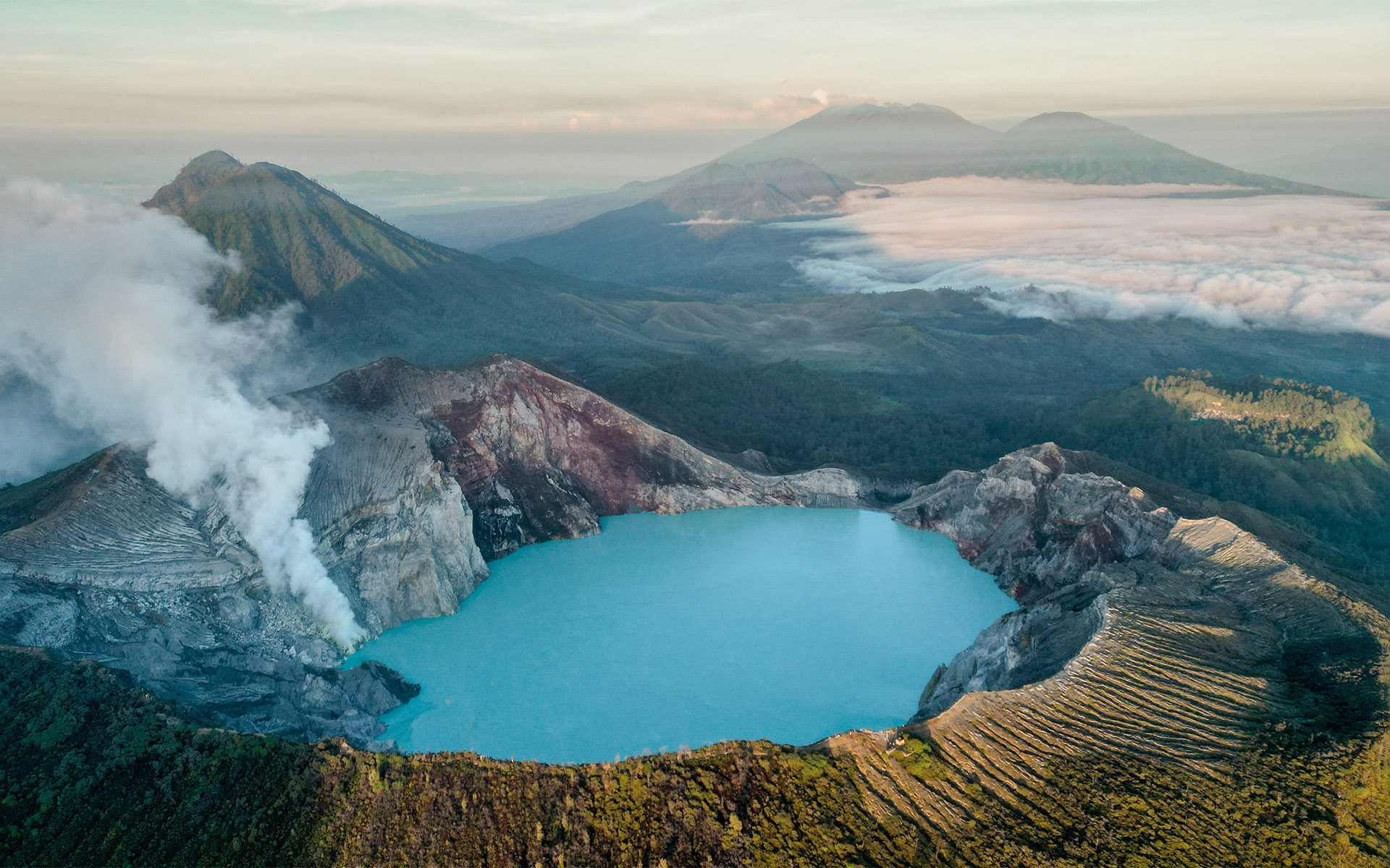 Ein türkisblauer See im Vulkan Ijen in Java, im Hintergrund begrünte Berge.