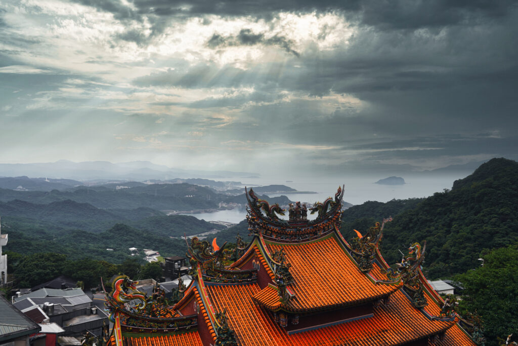 Blick von Jiufen über das rot gedeckte und mit Drachenskulpturen verzierte Tempeldach auf die Nordküste Taiwans.