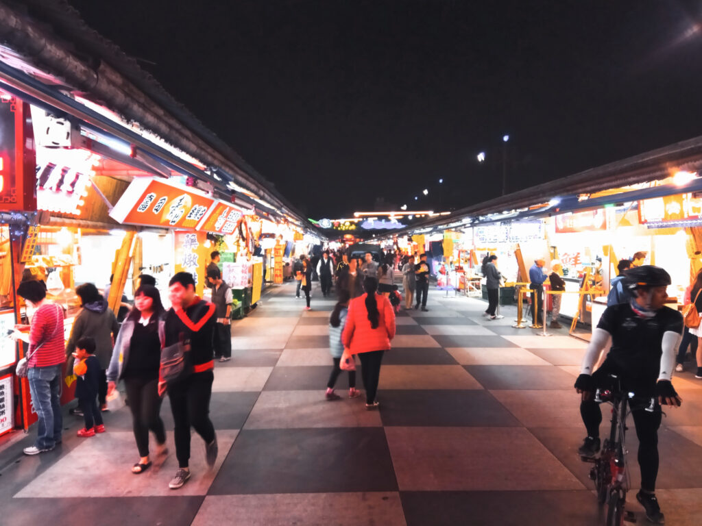Menschen schlendern in der Nacht über den bunt beleuchteten Dongdamen Nachtmarkt in Taiwan.