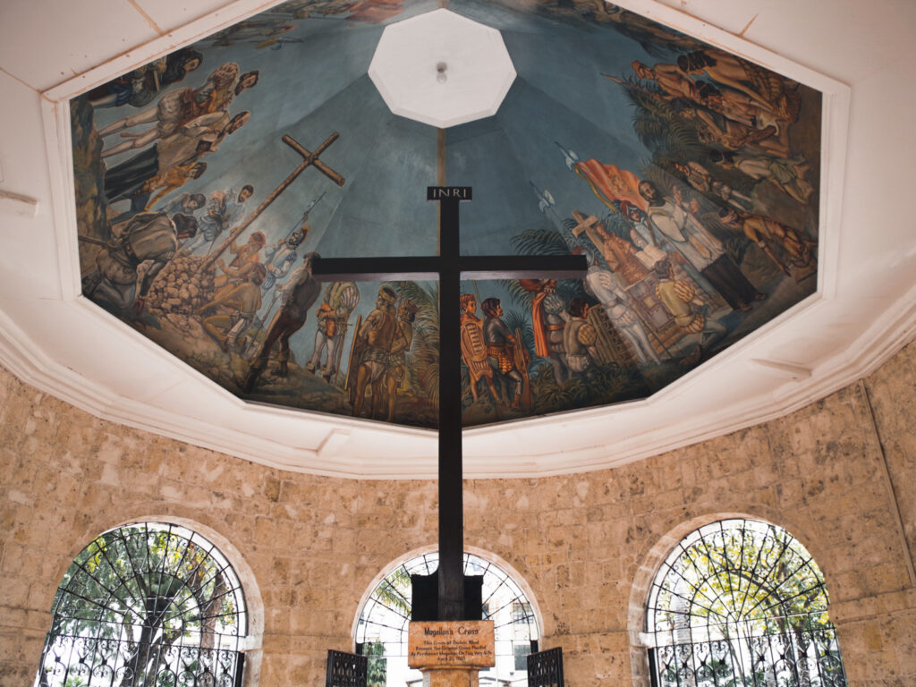 Ein großen Kreuz steht unter einem Pavillon mit einer prunkvollen Dekenmalerei.