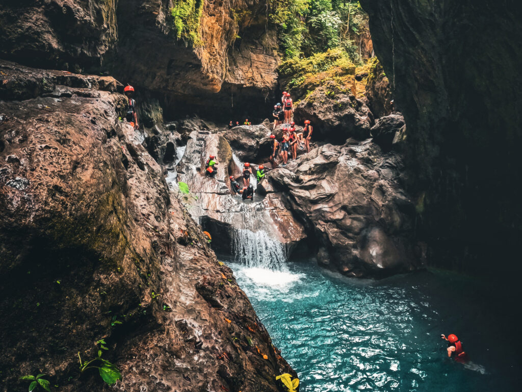 Menschen mit roten Helmen befinden sich an einem Wasserfall in der Schlucht.