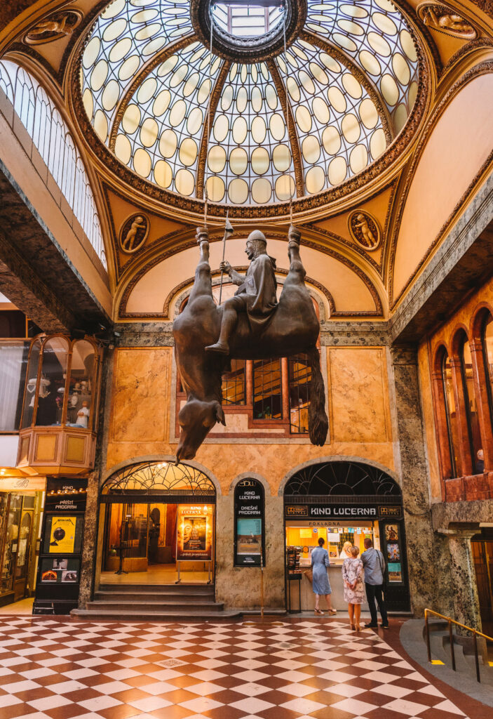 Ein kopfüberhängendes Pferd mit einem Reiter auf dem Bauch bildet das Denkmal der Wenzel-Statue in der Lucerna Passage in Prag.