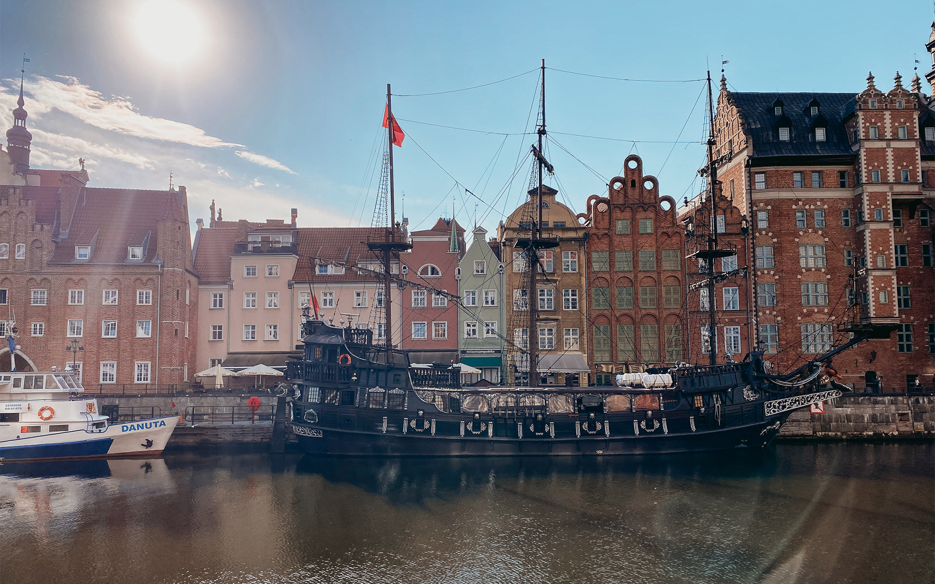 Ein altes Schiff steht im Wasser vor schönen, alten Reihenhäusern.