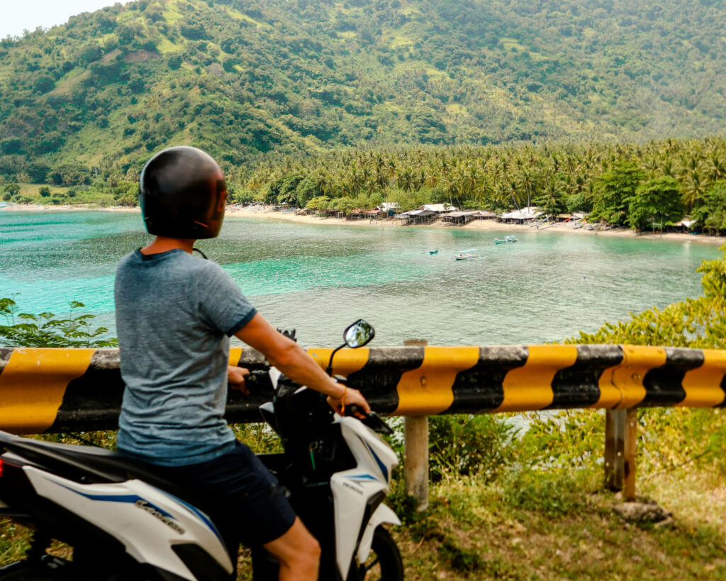 Reiseblogger Tom von Traveloptimizer genießt auf einem Roller die Aussicht auf den Strand Pandanan auf Lombok.