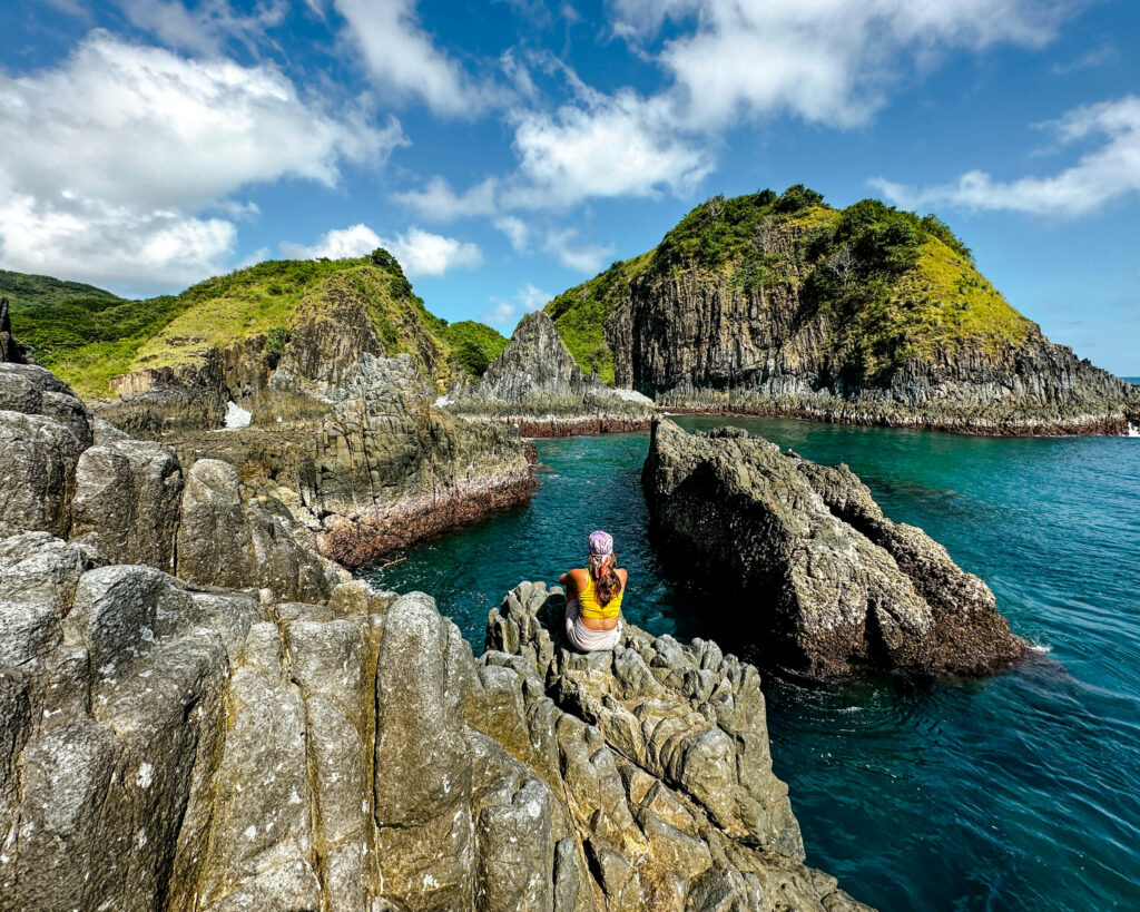 Reisebloggerin Nina von Traveloptimizer sitzt auf einem Basaltfelsen beim Semeti Beach, einem Strand auf Lombok.