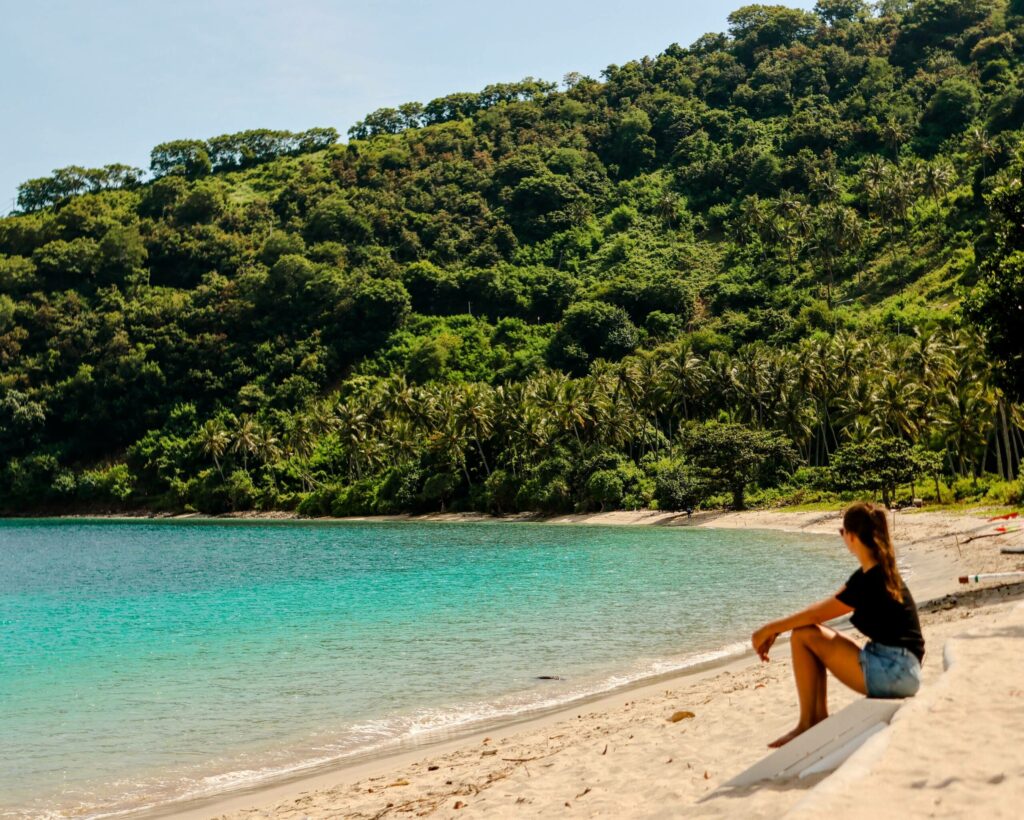 Reisebloggerin Nina von Traveloptimizer genießt an einem Sandstrand von Lombok den Blick auf das türkisblaue Meer.