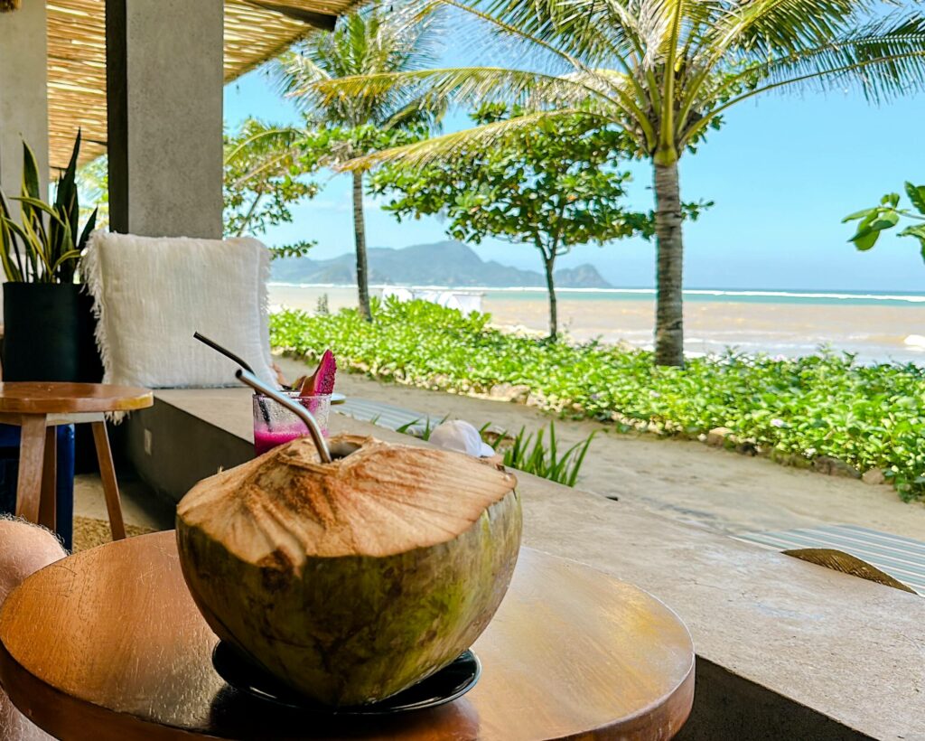 Der Blick aus einem Warung in Lombok auf das Meer, auf dem Tisch steht eine Kokosnuss mit Strohhalm.