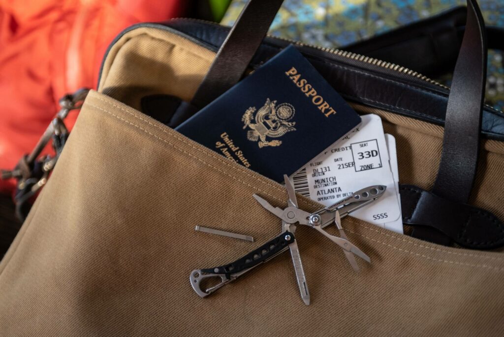 Ein nützlicher Begleiter auf Reisen: Das Multitool, das hier auf einer braunen Umhängetasche neben dem Reisepass und den Flugtickets liegt.